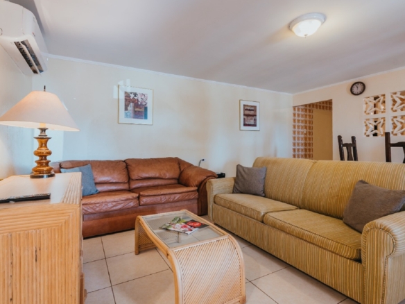 Living room area inside the 7 studio apartments in Aruba with two sofas, coffee table, wall-mounted TV, and dining area