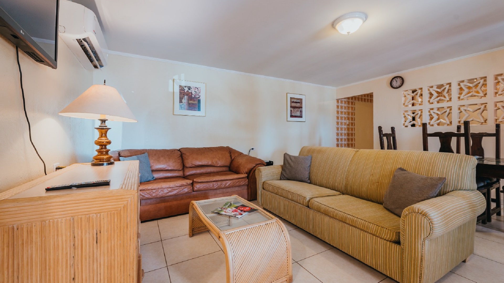 Living room area inside the 7 studio apartments in Aruba with two sofas, coffee table, wall-mounted TV, and dining area