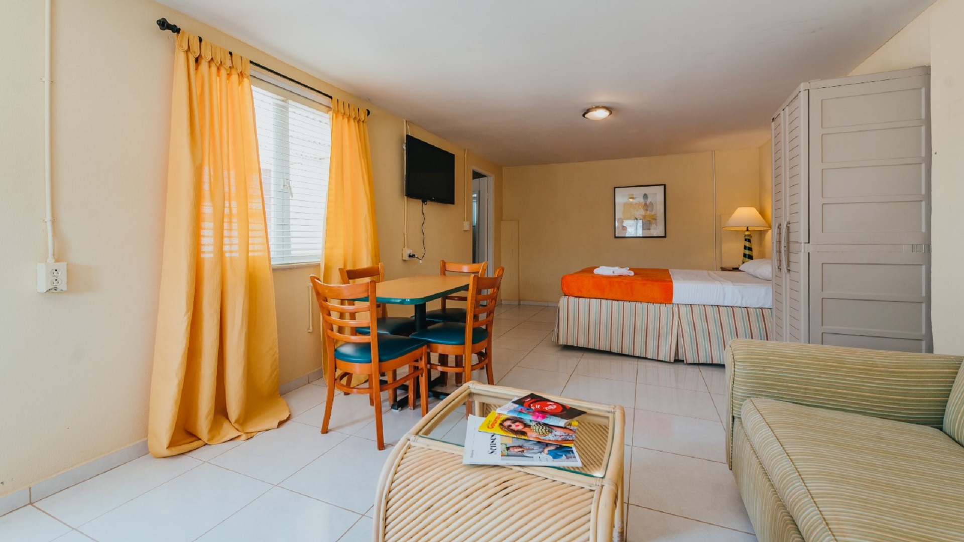 Interior of a studio apartment in Aruba with a bed, dining table, seating area, and tiled flooring