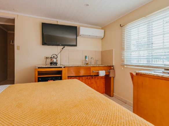 Studio room inside the 7 studio apartments in Aruba featuring a bed, kitchenette, sink area, TV, and air conditioning unit