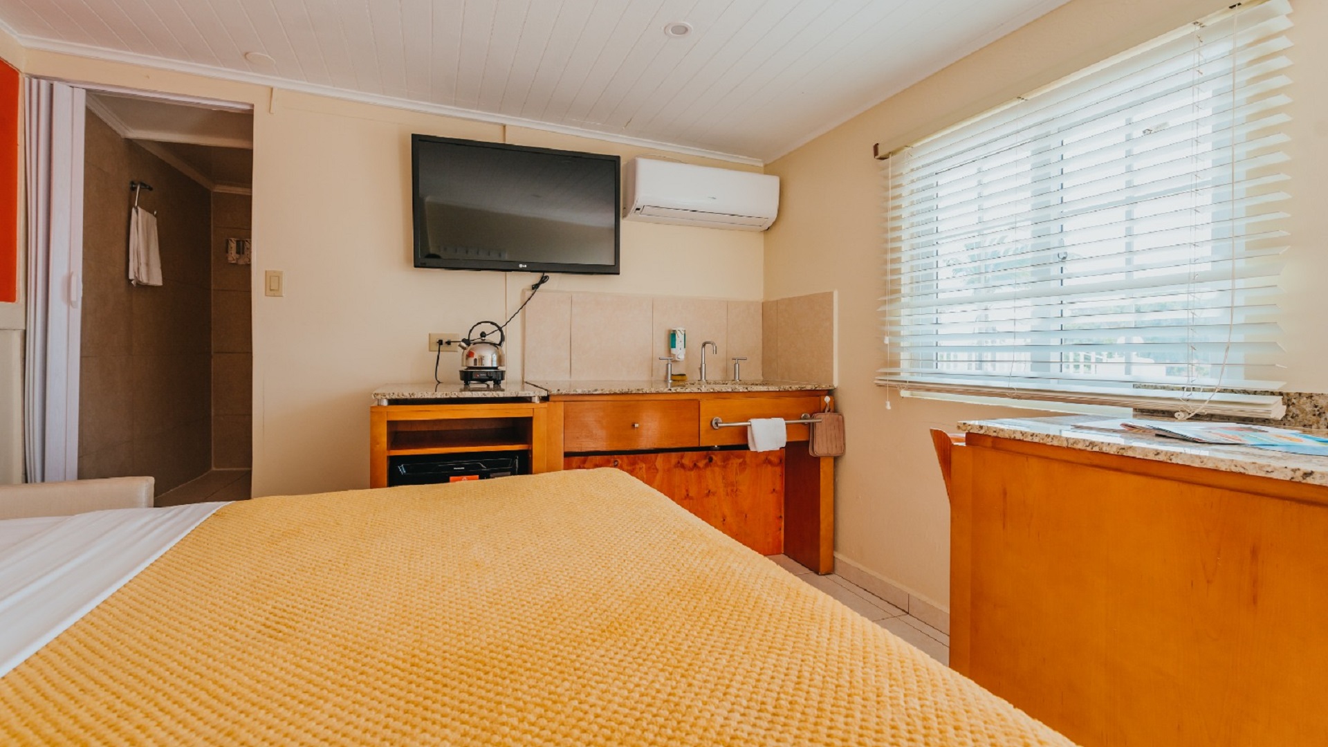 Studio room inside the 7 studio apartments in Aruba featuring a bed, kitchenette, sink area, TV, and air conditioning unit