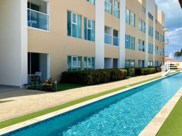 Poolside view of Aruba’s Life Garden 2 bedroom condo building and landscaped walkways in Aruba