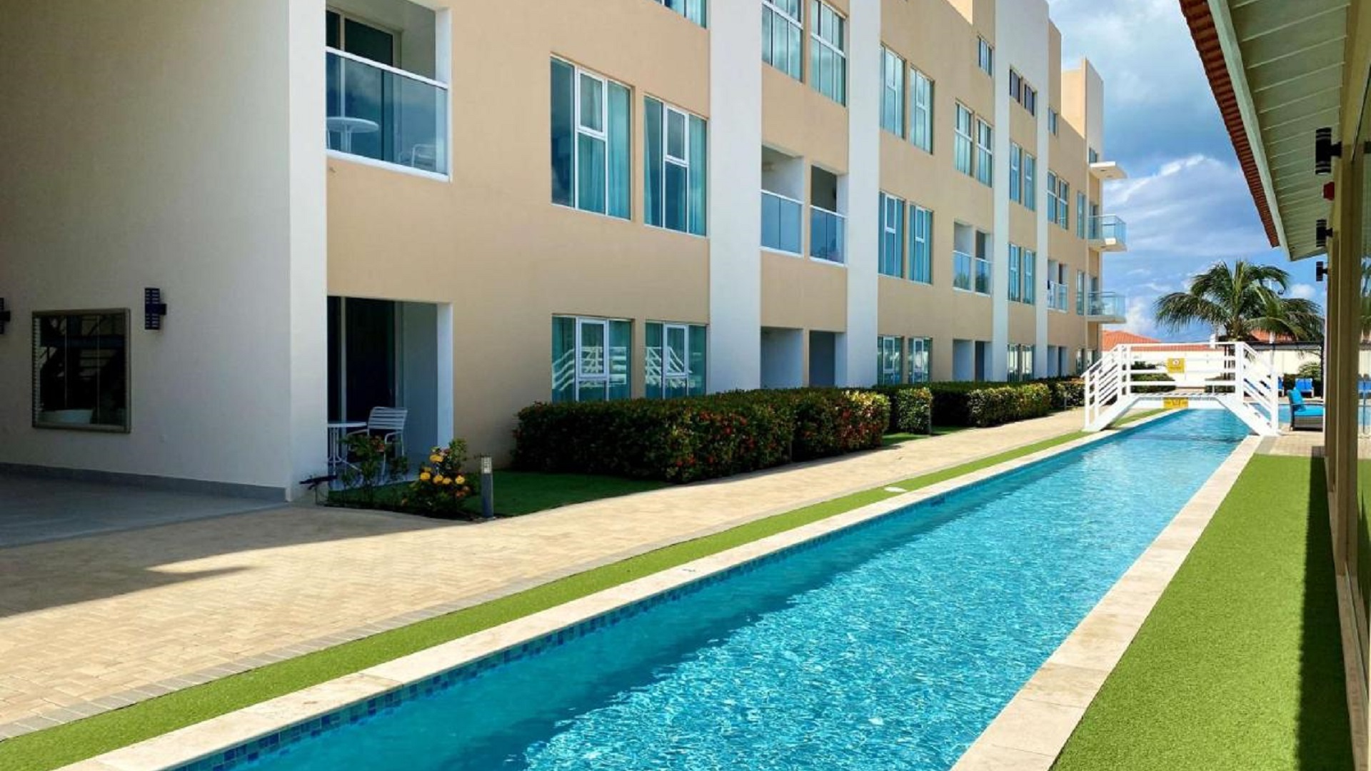 Poolside view of Aruba’s Life Garden 2 bedroom condo building and landscaped walkways in Aruba