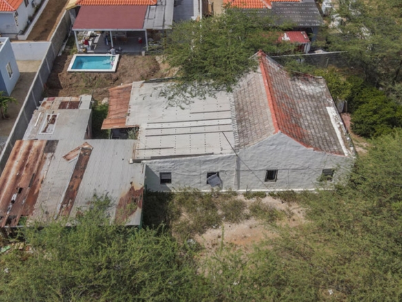 Top-down drone view of an existing building with attached structures and surrounding vegetation.