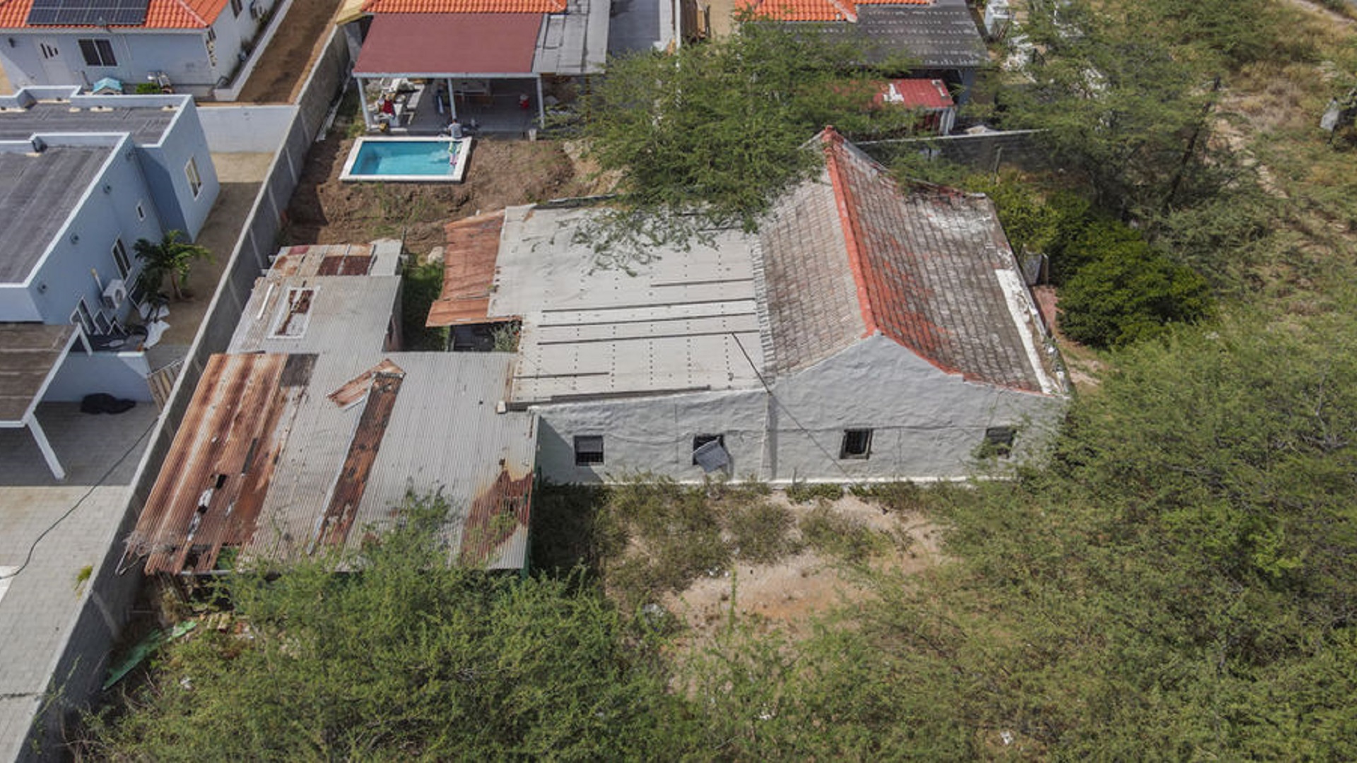 Top-down drone view of an existing building with attached structures and surrounding vegetation.