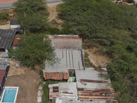 Overhead drone photograph of an existing property bordered by vegetation and nearby residential buildings.