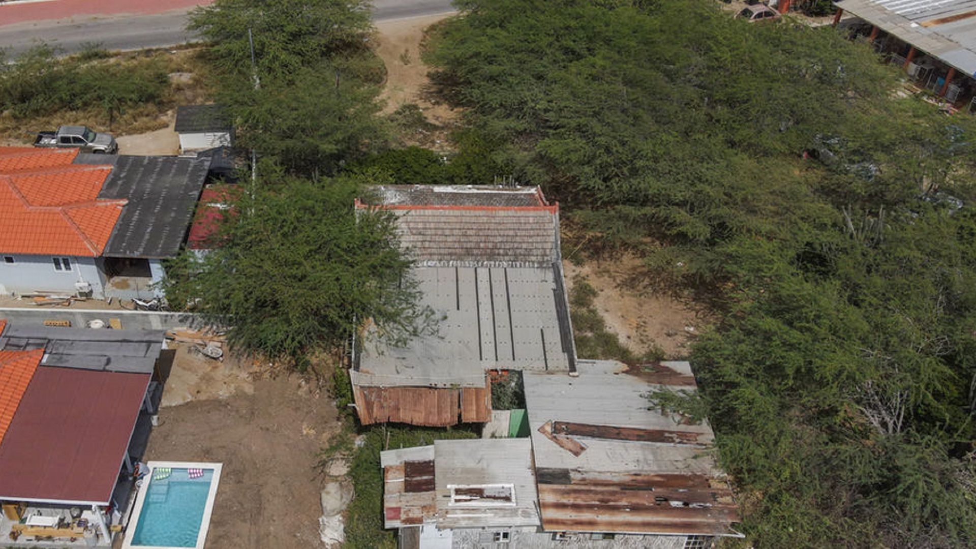 Overhead drone photograph of an existing property bordered by vegetation and nearby residential buildings.