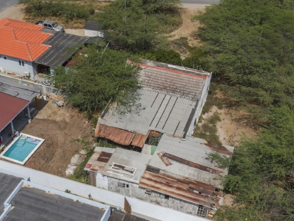Aerial site overview showing neighboring homes, vegetation, and an existing building.