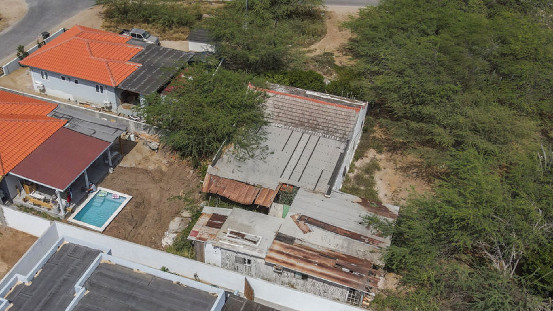 Aerial site overview showing neighboring homes, vegetation, and an existing building.