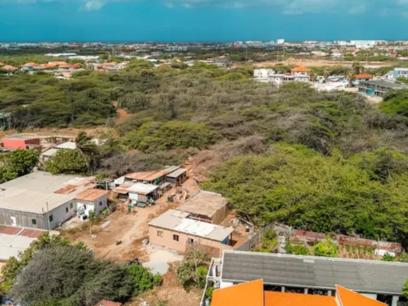 Aerial overview of development land for sale in Bubali, Noord, Aruba, showing surrounding residential properties, vegetation, and distant coastal skyline.