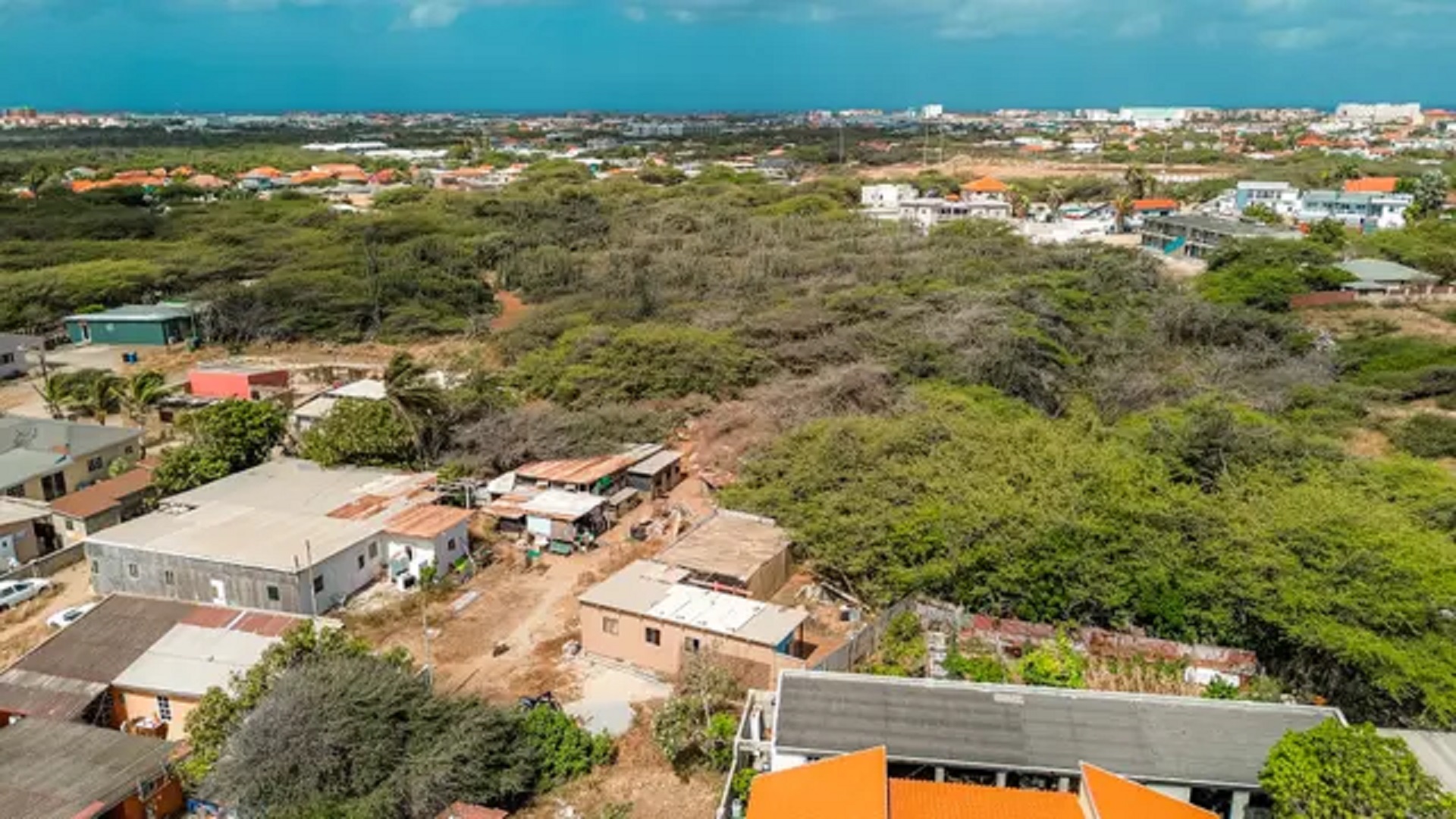 Aerial overview of development land for sale in Bubali, Noord, Aruba, showing surrounding residential properties, vegetation, and distant coastal skyline.