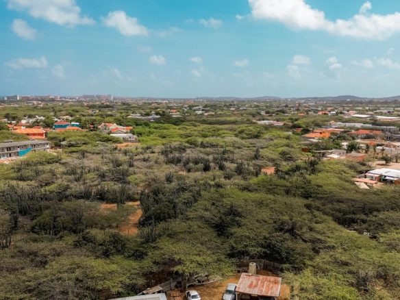 Aerial image of development land in Bubali, Noord, Aruba, showing road access, surrounding properties, and distant coastal buildings.