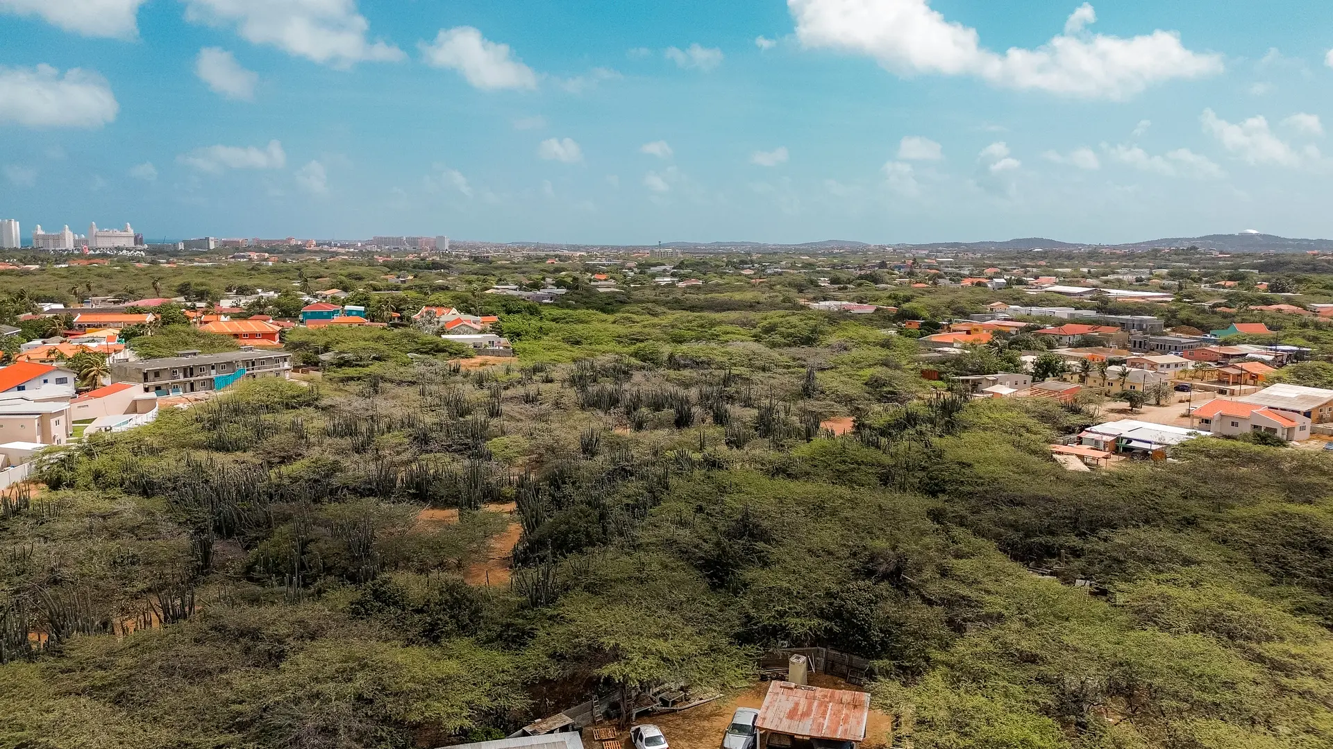 Aerial image of development land in Bubali, Noord, Aruba, showing road access, surrounding properties, and distant coastal buildings.