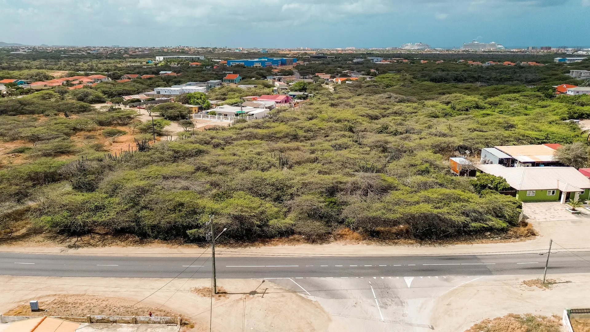 Aerial view of development land in Bubali, Noord, Aruba, showing road frontage, surrounding homes, and natural vegetation.