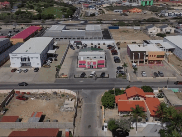 Front aerial view of the Commercial Office Space for Rent at Schotlandstraat 77-A Aruba showing the office building, parking lot, and neighboring commercial buildings.