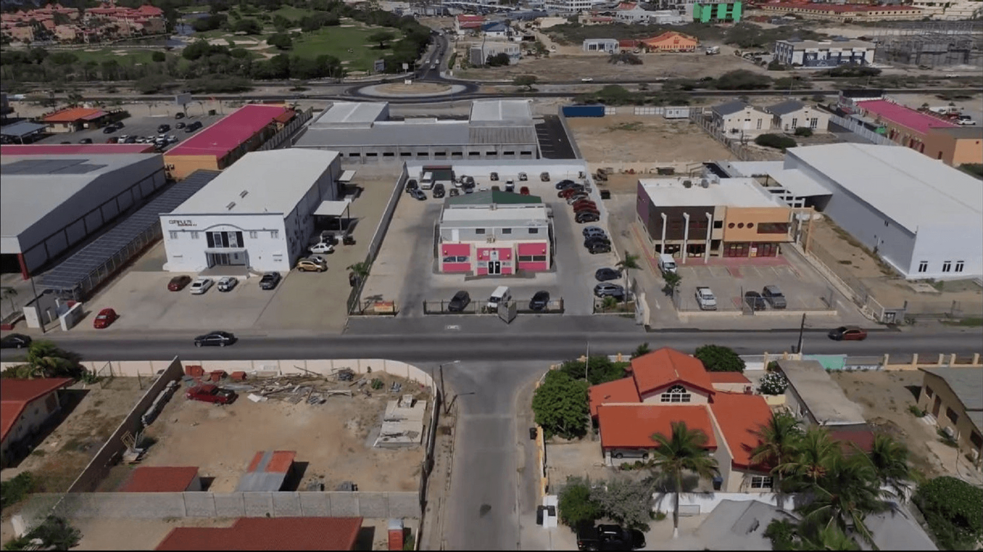 Front aerial view of the Commercial Office Space for Rent at Schotlandstraat 77-A Aruba showing the office building, parking lot, and neighboring commercial buildings.
