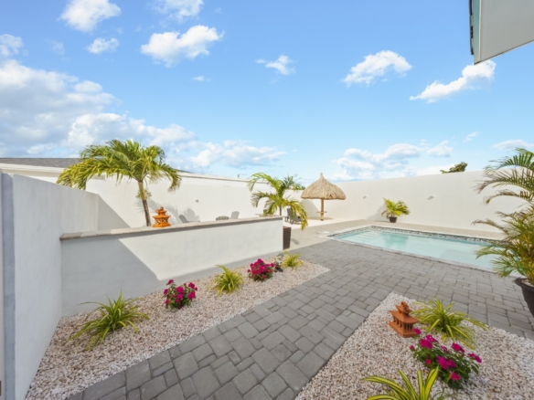 Private courtyard and swimming pool at Pos Abao 10 F villa in Noord, Aruba, featuring paved walkways, tropical landscaping, and high privacy walls.