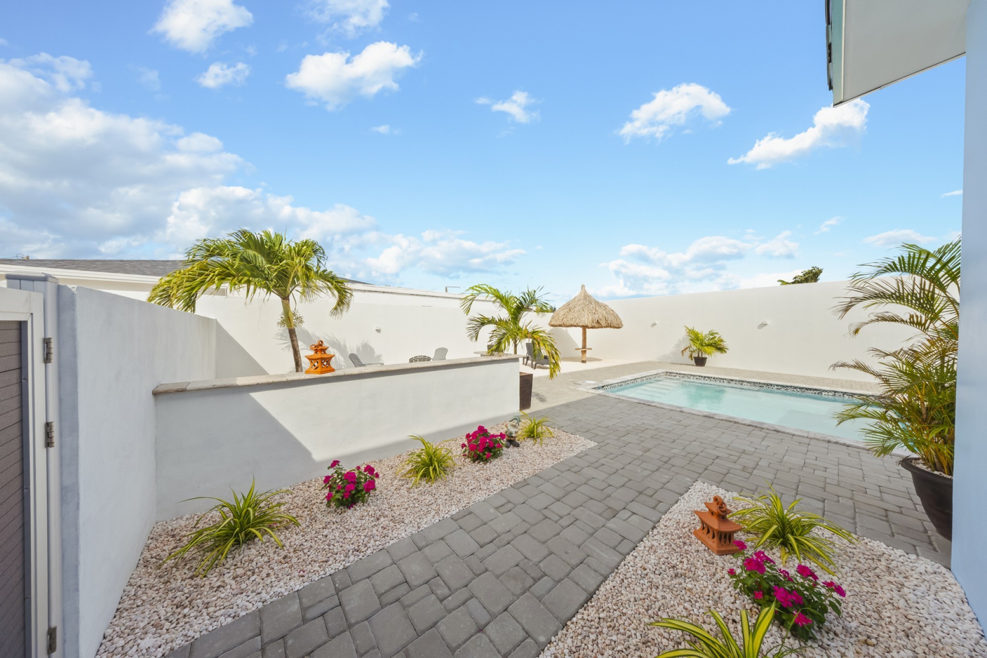 Private courtyard and swimming pool at Pos Abao 10 F villa in Noord, Aruba, featuring paved walkways, tropical landscaping, and high privacy walls.