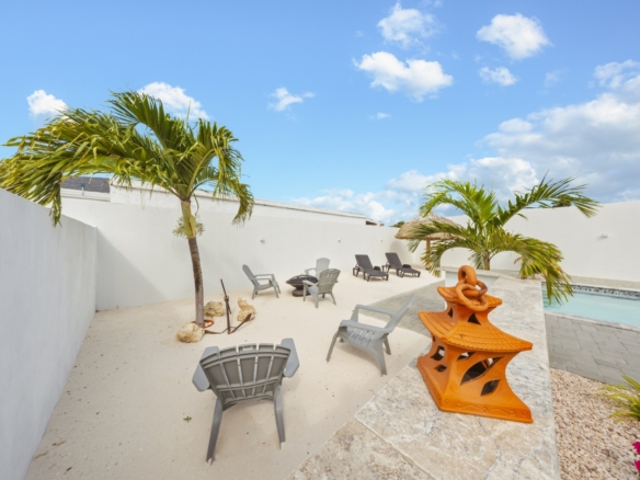Poolside seating area with palm trees and lounge chairs at the Pos Abao 10 F villa in Noord, Aruba.