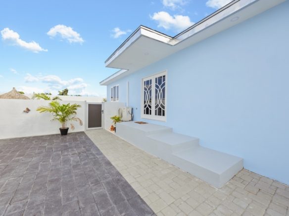 Exterior side view of the Pos Abao 10 F villa showing entry steps and paved courtyard in Noord, Aruba.