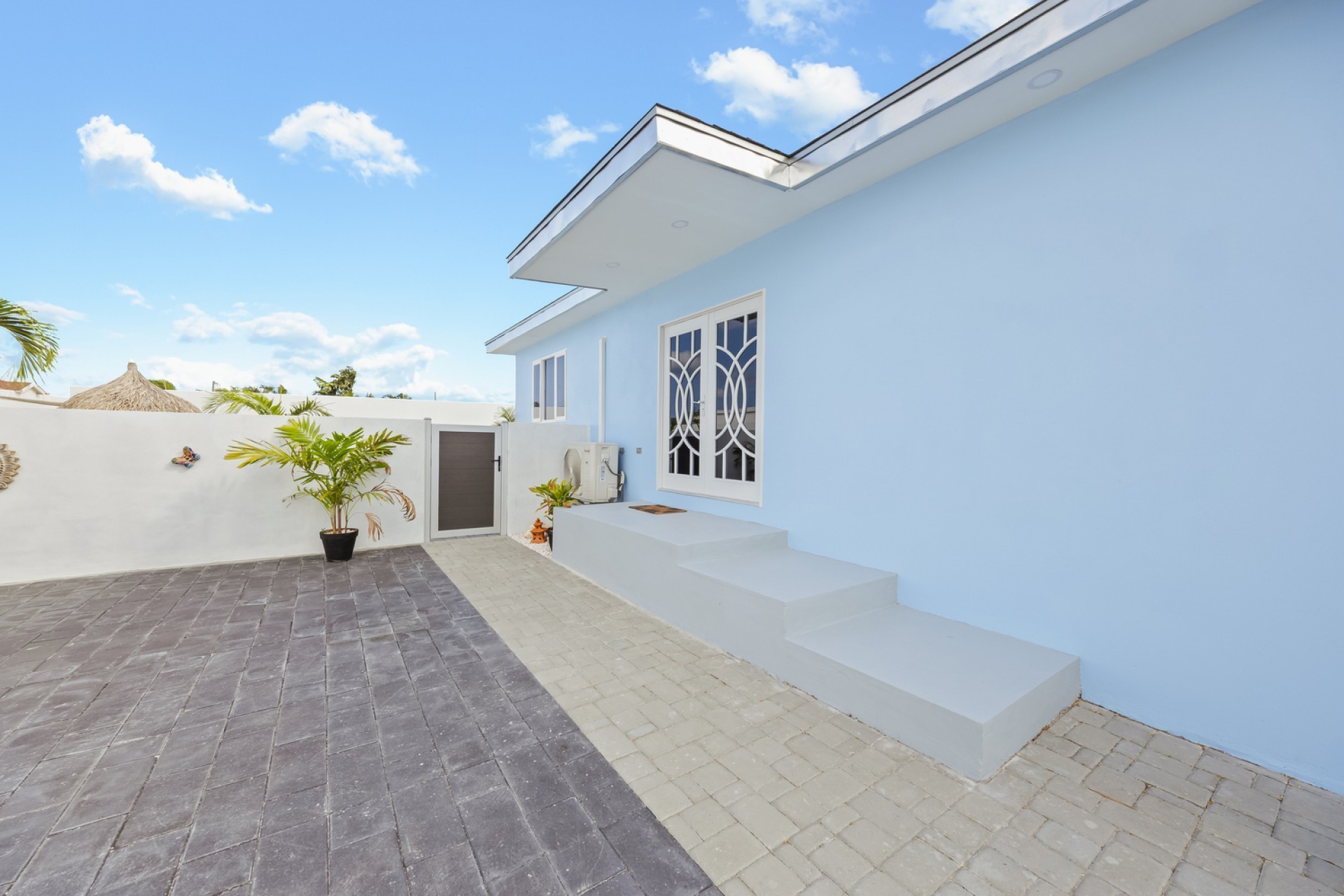 Exterior side view of the Pos Abao 10 F villa showing entry steps and paved courtyard in Noord, Aruba.