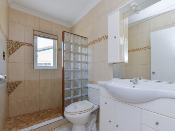 Modern bathroom with glass block shower divider, tiled walls, vanity sink, and toilet in Tanki Leendert 123-B Aruba.