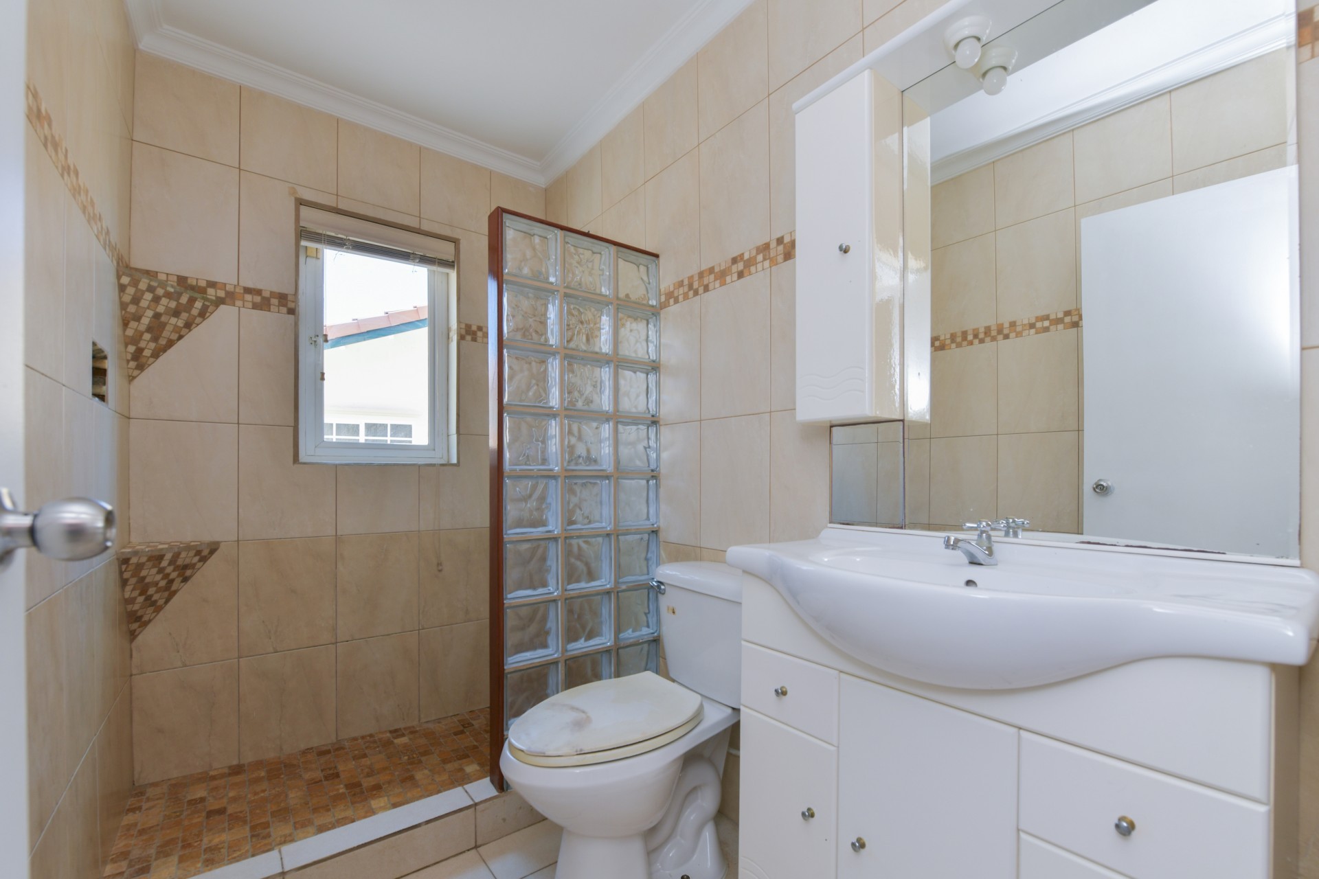 Modern bathroom with glass block shower divider, tiled walls, vanity sink, and toilet in Tanki Leendert 123-B Aruba.