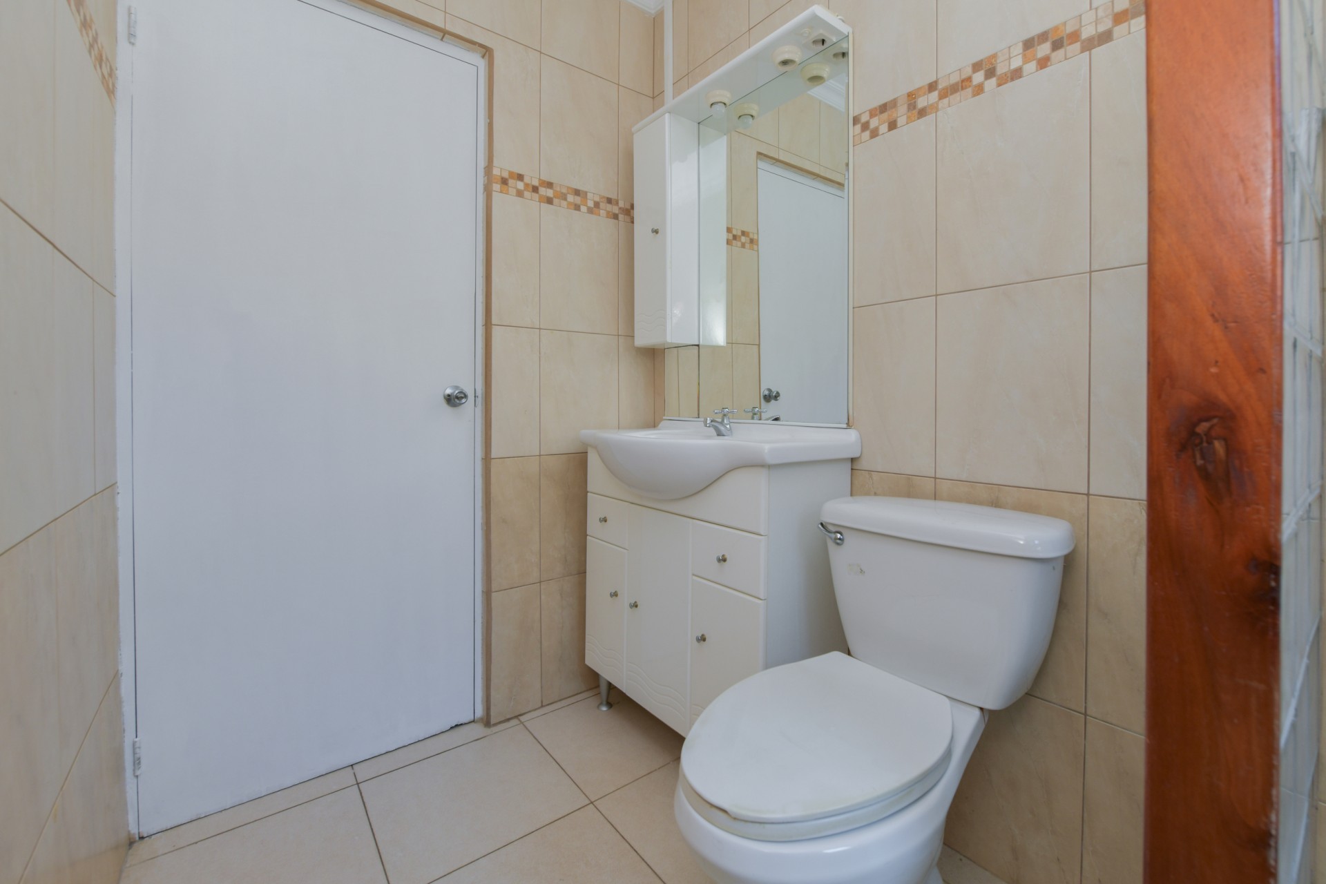 Bathroom vanity with sink, mirror cabinet, and toilet in a clean tiled bathroom in Aruba.