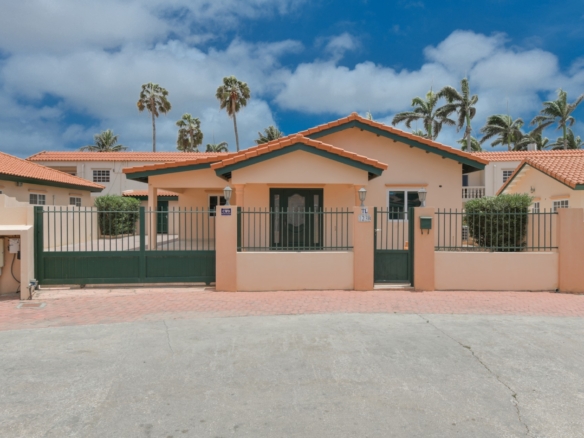 Front view of a 3-bedroom home for sale in Tanki Leendert Aruba with gated entrance, covered porch, and landscaped surroundings.