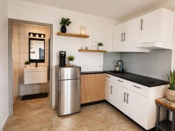 Compact kitchen in an Aruba vacation rental with white cabinets, a refrigerator, open shelving, and a sink.